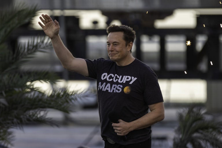 Elon Musk waves and wears an "Occupy Mars" t-shirt.