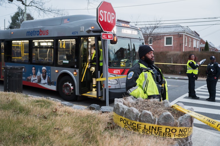 Police officers stand near a metrobus and some yellow police tape.