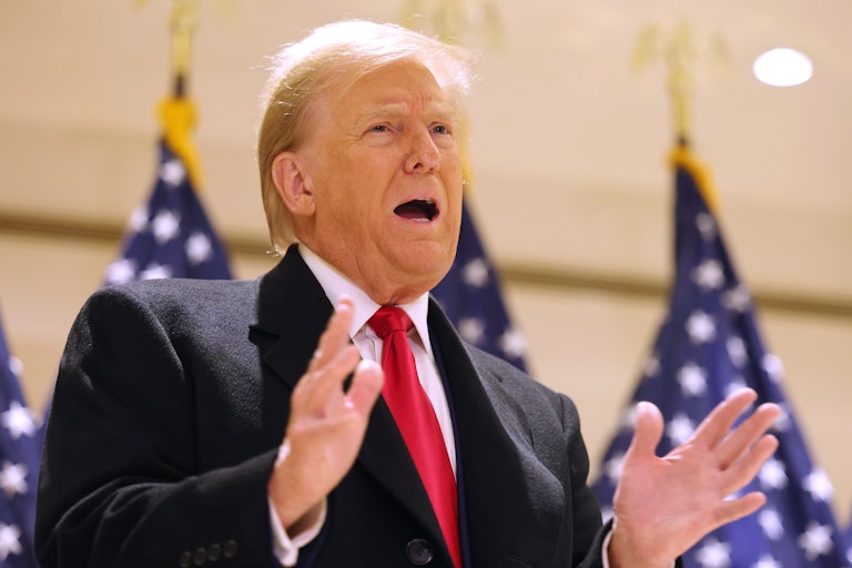 Donald Trump gestures while standing in front of American flags