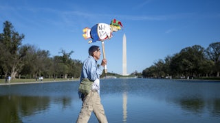 A protester walks past the Reflecting Pool, opposite the Washington Monument, holding up a drawing of Donald Trump that says, "Not a king"
