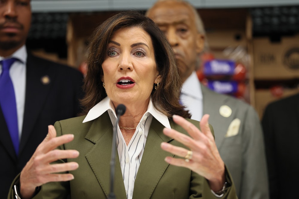 Kathy Hochul gestures with both hands while speaking into a microphone, with others behind her.