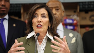 Kathy Hochul gestures with both hands while speaking into a microphone, with others behind her.