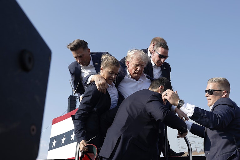 Donald Trump being held up by Secret Service after being shot. He has blood on the right side of his face.