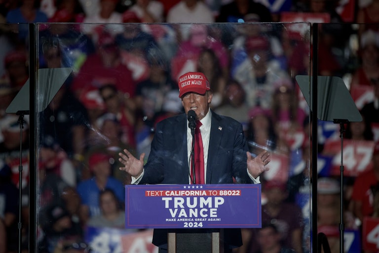 Donald Trump gestures and speaks while standing behind bulletproof glass during his rally in Coachella, California