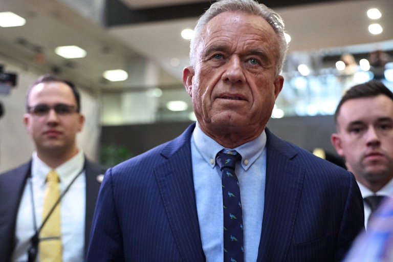 Robert F. Kennedy Jr., looking like a dang cooked ham, walks flanked by two staffers