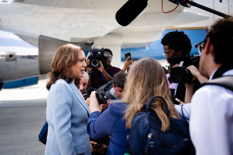 Kamala Harris talks to reporters on a tarmac.