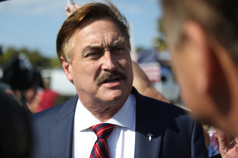 Mike Lindell surrounded by a crowd. He looks angry at another person.