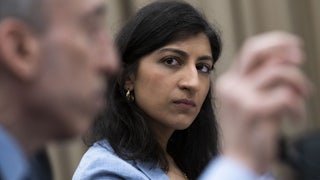 Federal Trade Commissioner Lina Khan looks at a white man (out of focus) speaking next to her