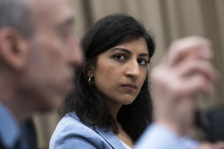 Federal Trade Commissioner Lina Khan looks at a white man (out of focus) speaking next to her