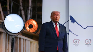 Donald Trump puckers his lips while standing on stage at the G7 summit