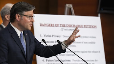 House Speaker Mike Johnson, seen in profile, holds out a hand while speaking at a podium