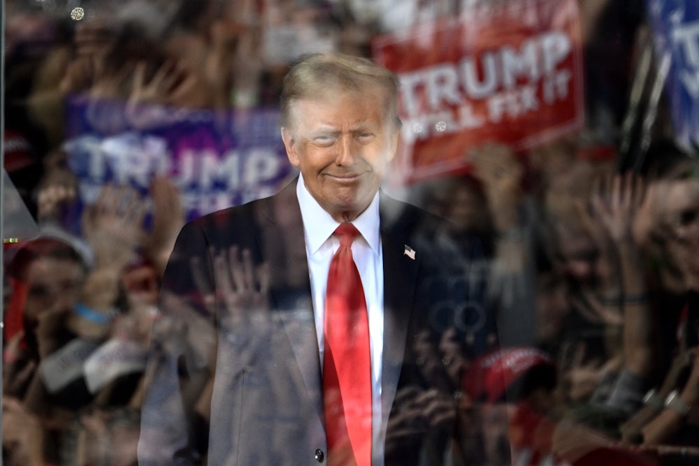 Trump is seen through bulletproof glass with the reflections of cheering fans in the glass.