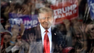 Trump is seen through bulletproof glass with the reflections of cheering fans in the glass.
