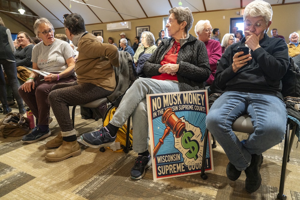 A member of the crowd at a "People v. Musk Grassroots Town Hall" hosted by the Democratic Party of Wisconsin at the library in Sauk City, Wisconsin has a sign that reads "NO MUSK MONEY IN THE WISCONSIN SUPREME COURT."