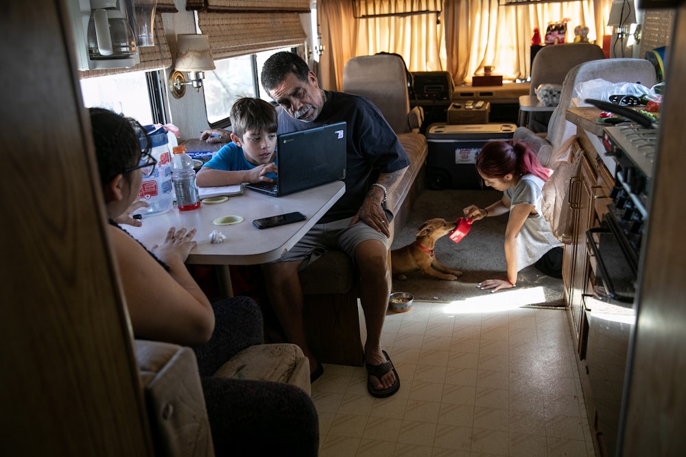 Inside an RV, a father helps his son with homework while his two daughters sit nearby.