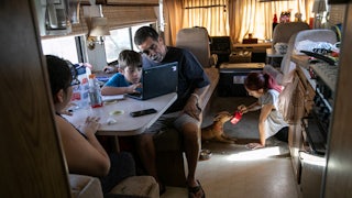 Inside an RV, a father helps his son with homework while his two daughters sit nearby.