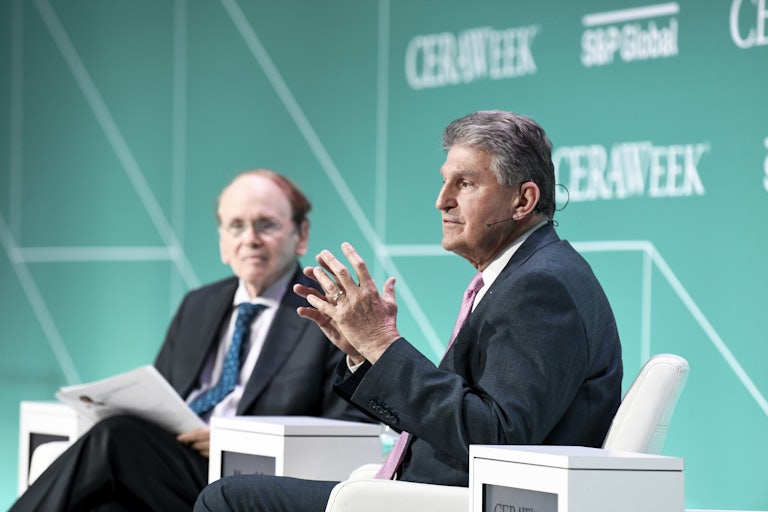 Senator Joe Manchin speaks while seated, with another seated man in the background.