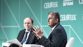 Senator Joe Manchin speaks while seated, with another seated man in the background.