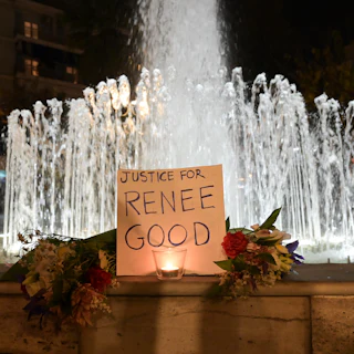 A sign that says, "Justice for Renee Good" and two bouquets stand in front of a fountain