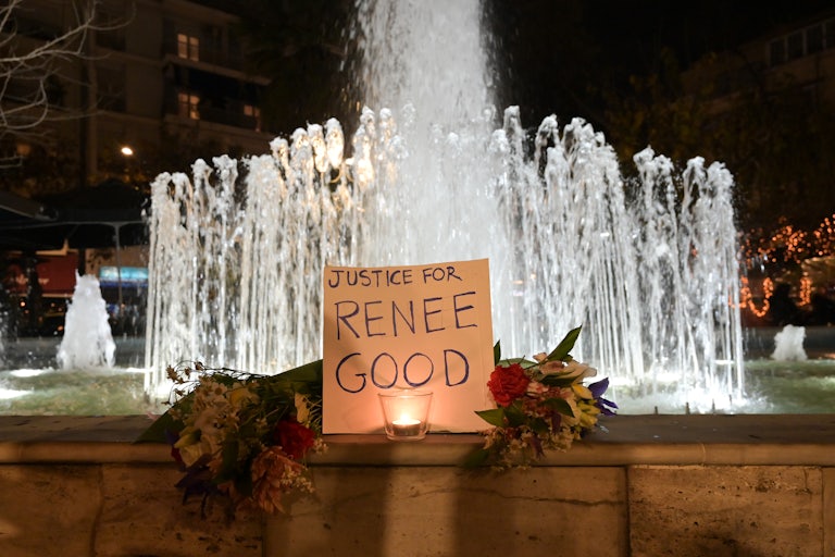 A sign that says, "Justice for Renee Good" and two bouquets stand in front of a fountain