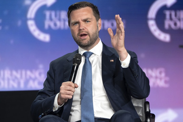 J.D Vance, seated, speaks with a mic in one hand and making raising the other for emphasis