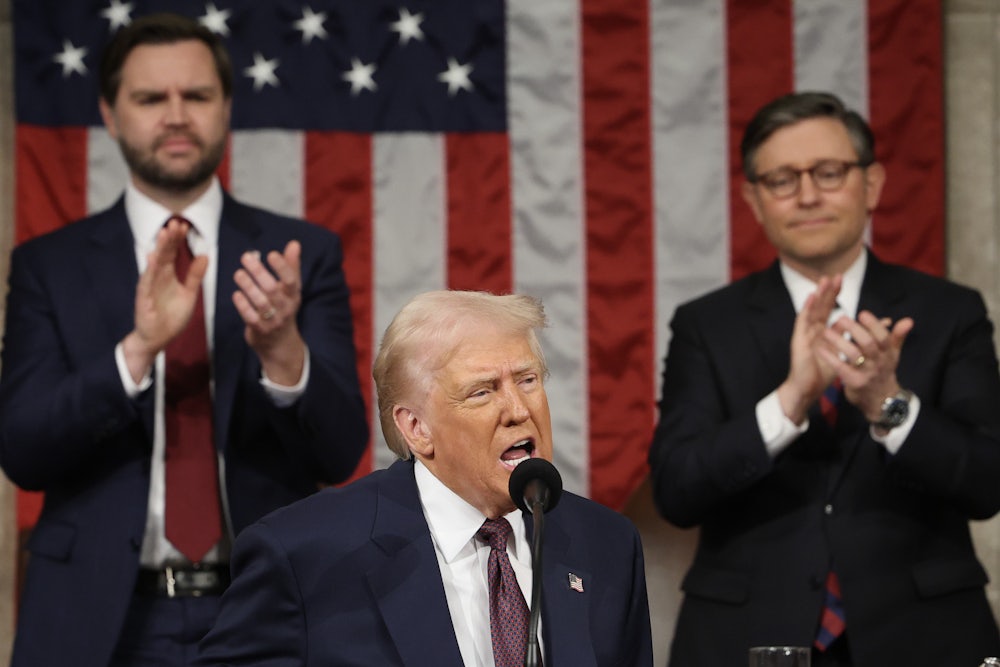 Donald Trump speaks into a microphone, with JD Vance and Mike Johnson clapping behind him, against the backdrop of an American flag.