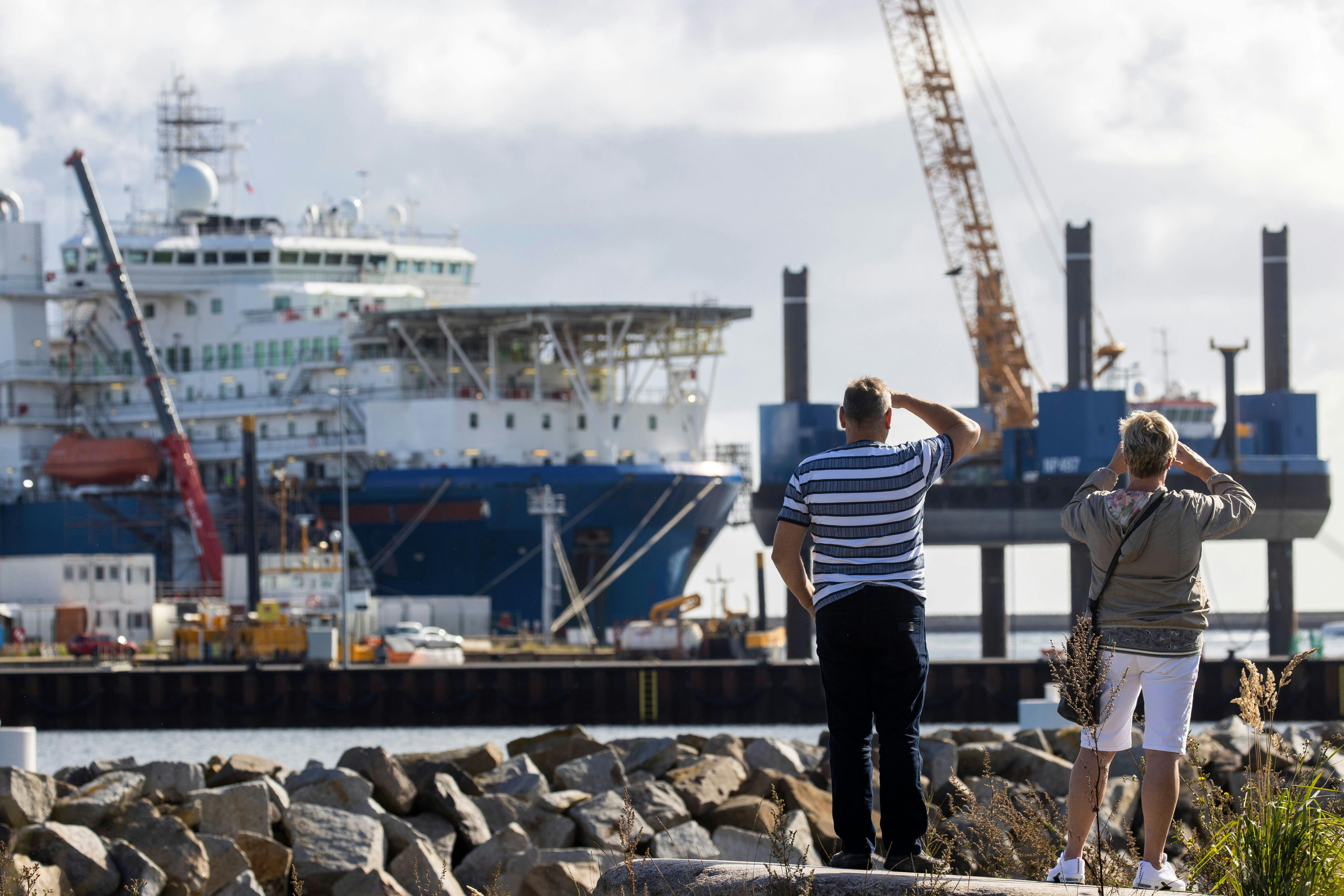 A couple takes pictures of a Russian pipe laying vessel on the island of Ruegen, Germany, as the ship waits to continue work on the Nord Stream 2 natural gas pipeline.