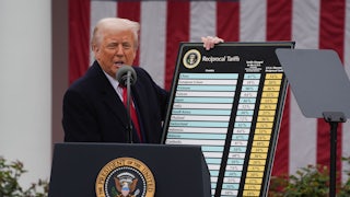 Donald Trump stands at the presidential podium and holds up a giant chart with a list of countries and the tariff rates.