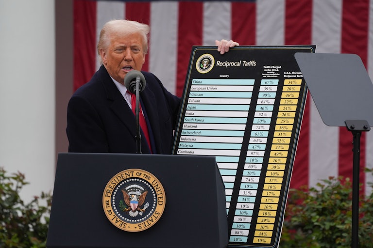 Donald Trump stands at the presidential podium and holds up a giant chart with a list of countries and the tariff rates.