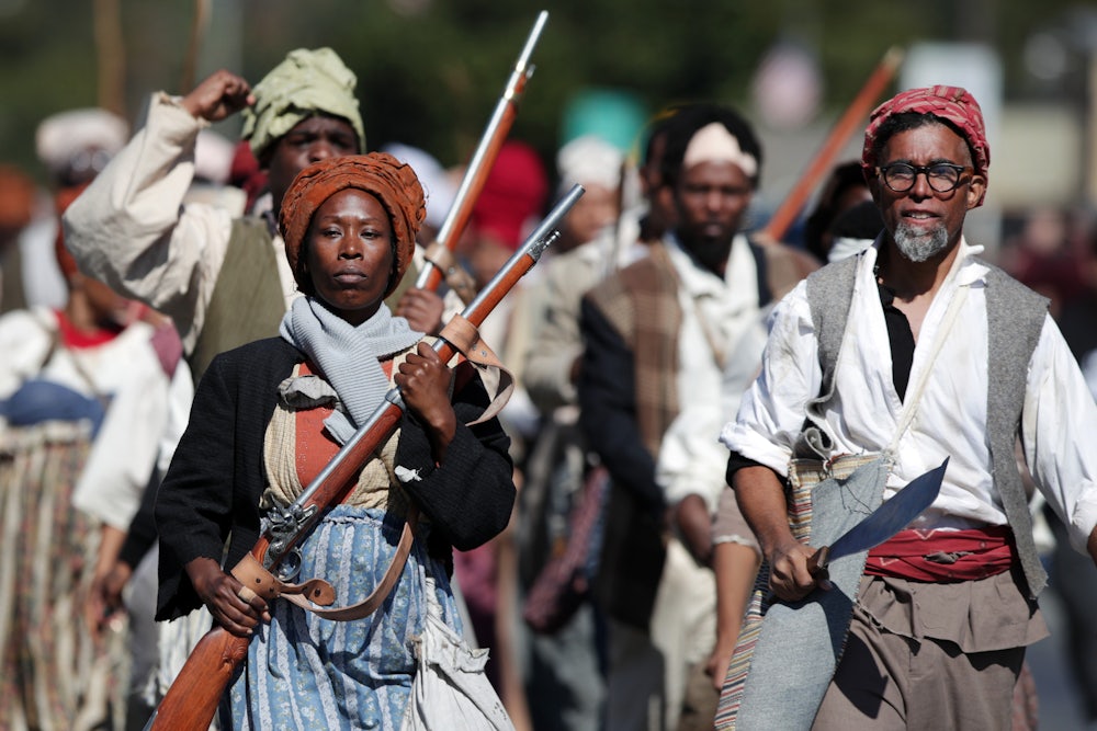 People in historical costumes walk forward carrying historically accurate firearms and other weapons.