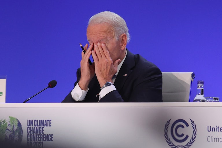 Joe Biden, seated at a table, rubs his eyes.