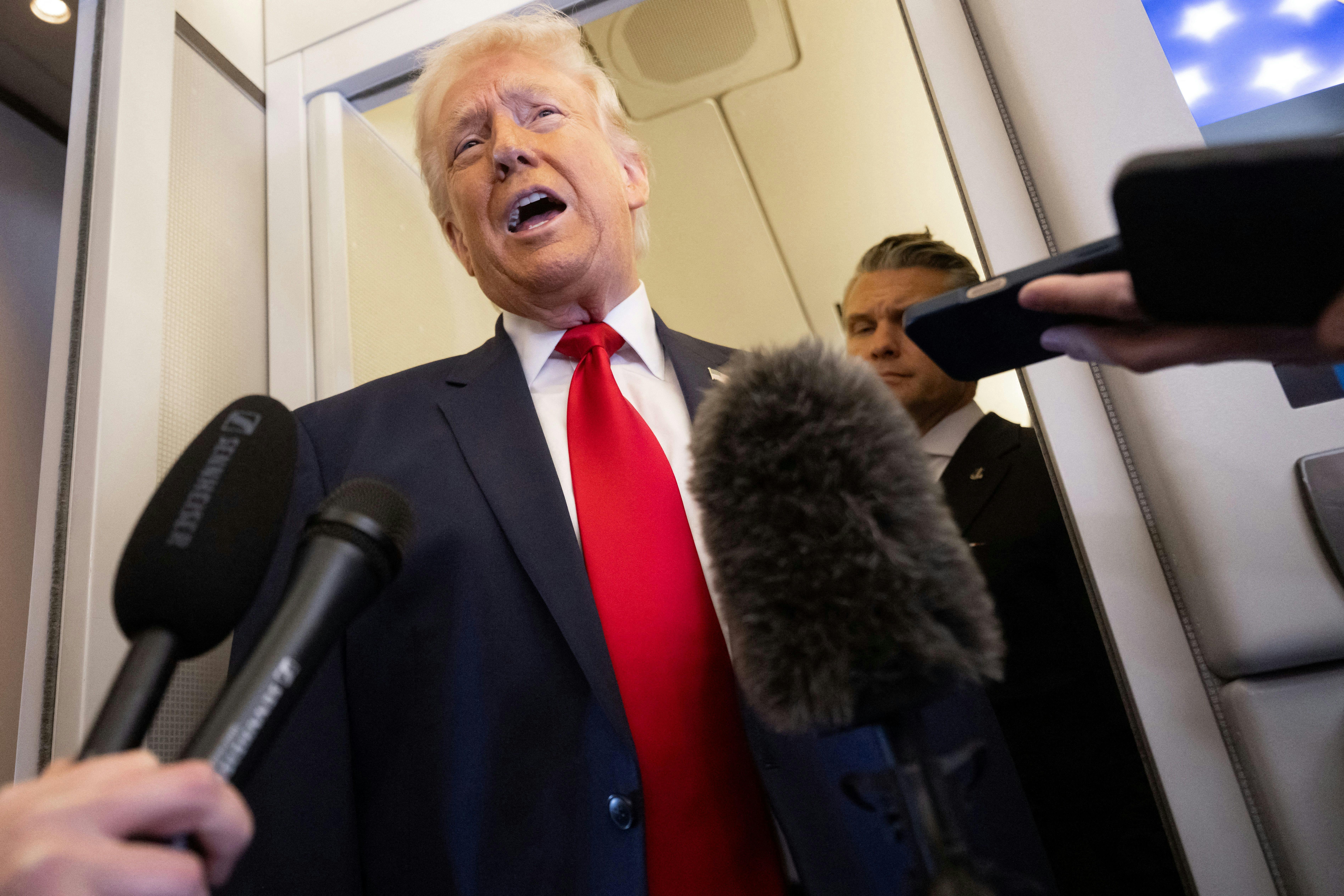 President Donald Trump speaks with the media as Defense Secretary Pete Hegseth looks on aboard Air Force One
