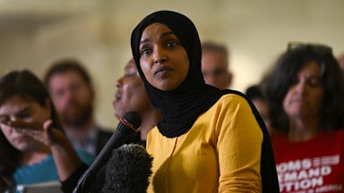 Representative Ilhan Omar speaks at a mic as others stand behind her.