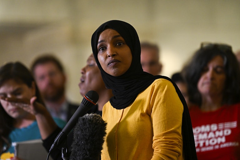 Representative Ilhan Omar speaks at a mic as others stand behind her.