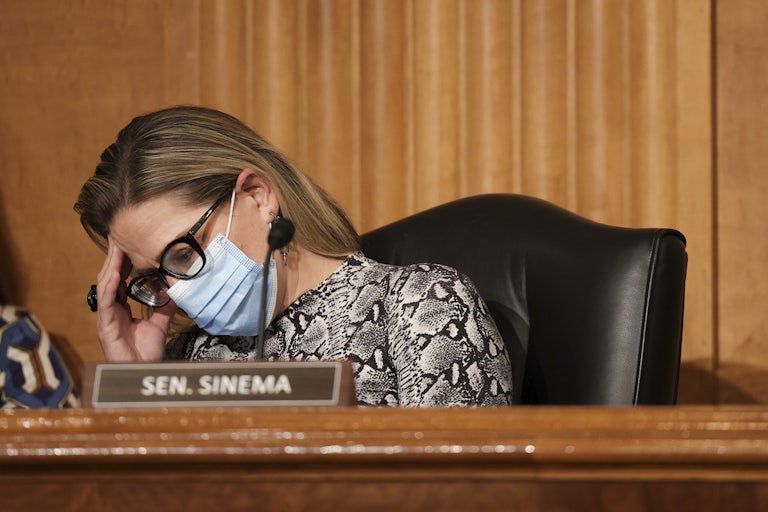 A masked Kyrsten Sinema puts her head in her hands during a hearing on Capitol Hill.