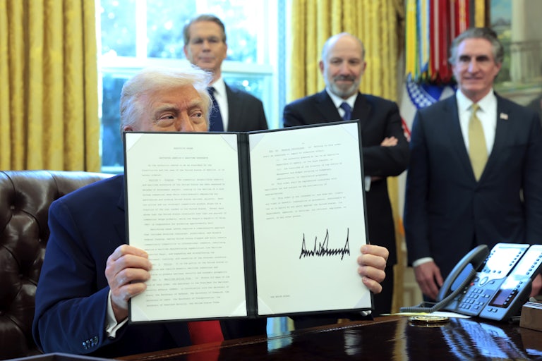 Donald Trump peeks behind a signed executive order he holds in front of his face in the White House. Scott Bessent, Howard Lutnick, and Doug Burgum smile in the background.