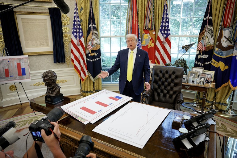 President Donald Trump speaks in front of posters depicting household income data in the Oval Office. Trump fired Bureau of Labor Statistics Commissioner Dr. Erika McEntarfer on August 1, claiming the agency issued “phony” jobs numbers during the Biden administration.
