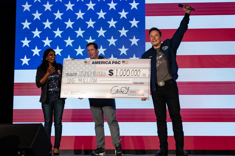 Elon Musk hands a giant $1 million check to Judey Kamora on a stage.
