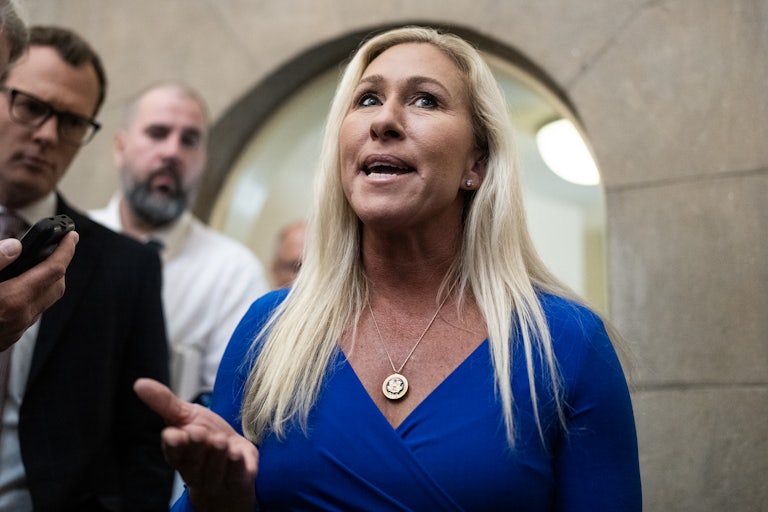 Marjorie Taylor Greene speaks and gestures with her hand as reporters surround her