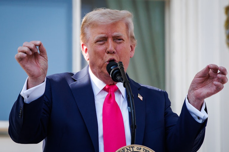 Donald Trump speaks at the presidential podium and raises both hands as if conducting an orchestra.