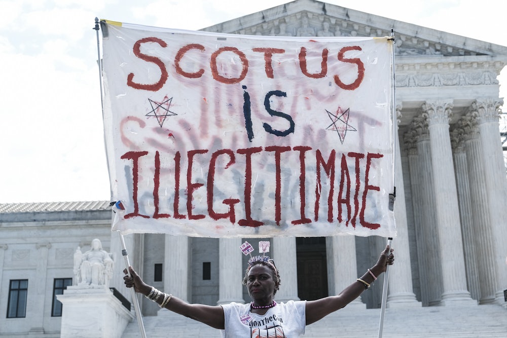 A woman hold a banner reading "SCOTUS is illegitimate" outside of the U.S. Supreme Court.