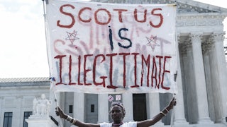 A woman hold a banner reading "SCOTUS is illegitimate" outside of the U.S. Supreme Court.