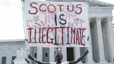 A woman hold a banner reading "SCOTUS is illegitimate" outside of the U.S. Supreme Court.