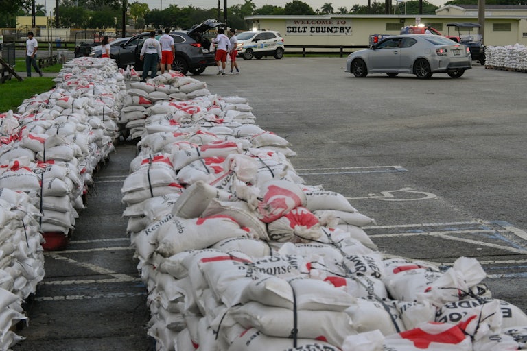 Two rows of sandbags piled up in a parking lot. A building in the back reads "Welcome to Colt County."