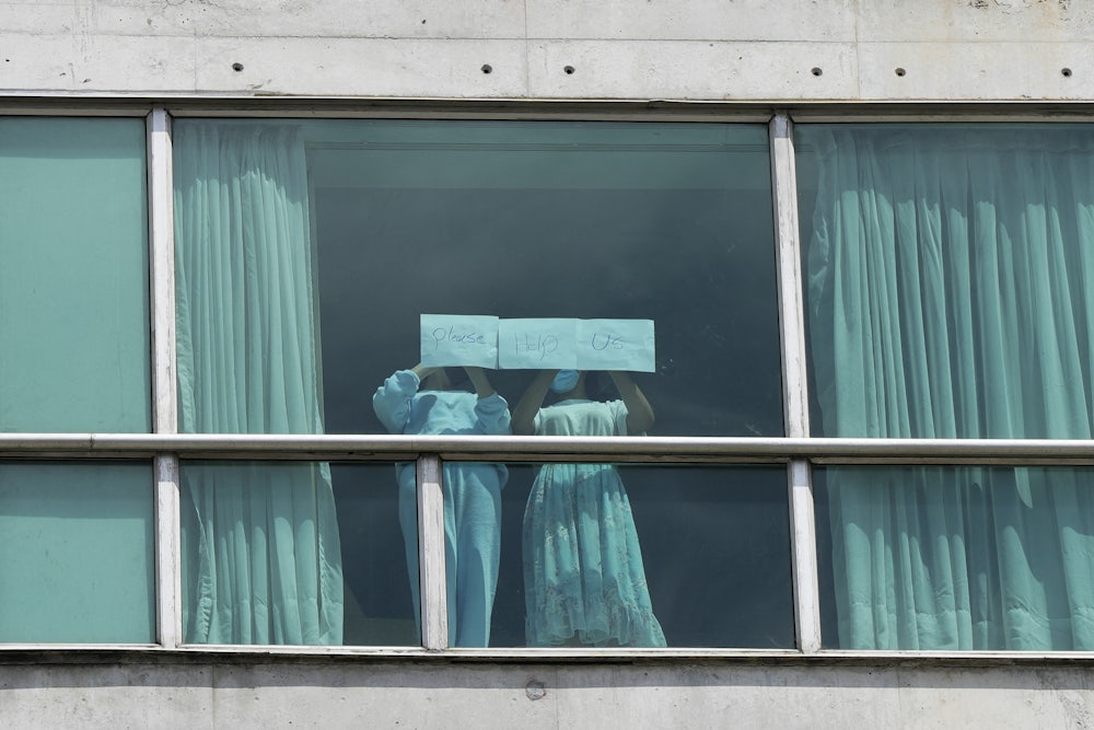 Two girls hold up a sign reading "Please help us" in a hotel window