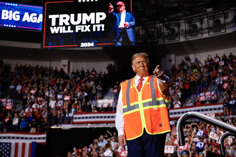 Donald Trump wears an orange construction vest and points at one of his campaign rallies