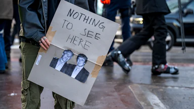 A protester holds a sign that says, "Nothing to see here" with a photo of Donald Trump and Jeffrey Epstein underneath