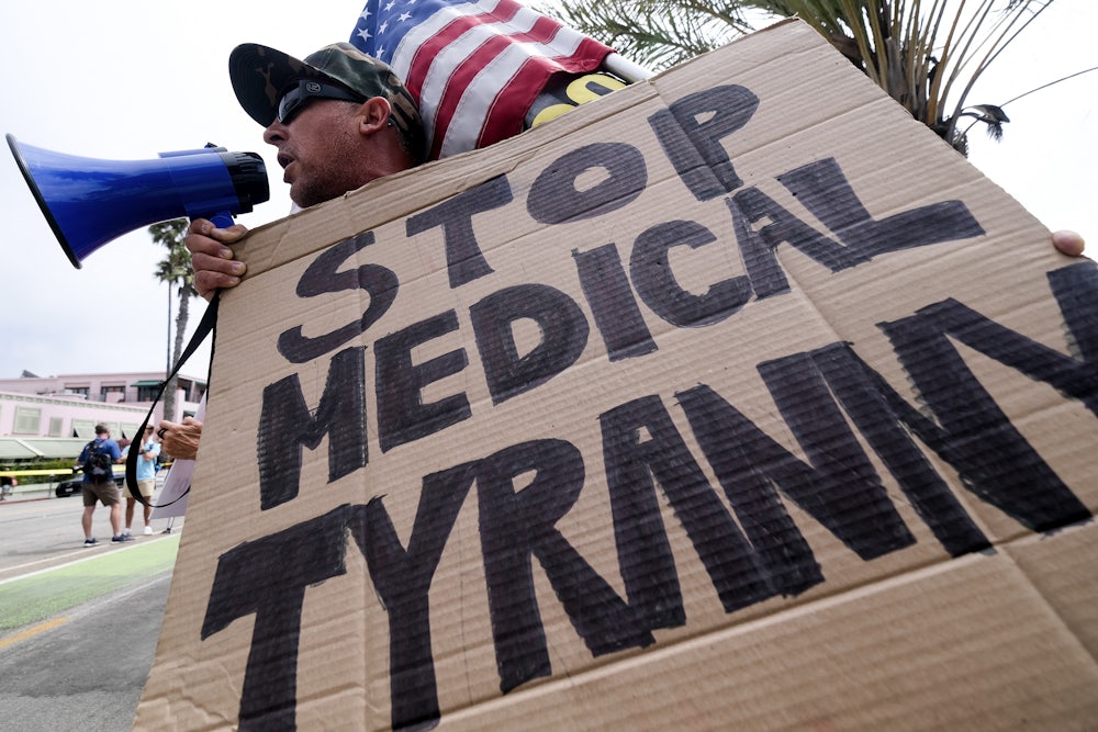 An anti-vaccination protester holds a sign and a flag as he takes part in a rally against Covid-19 vaccine mandates.