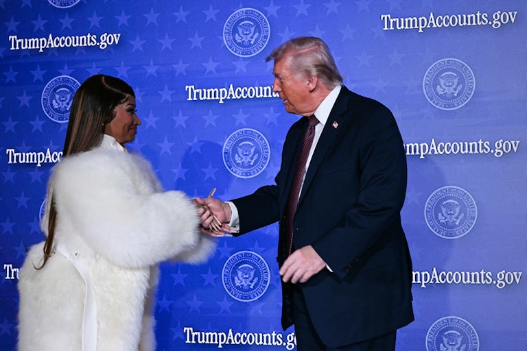 Nicki Minaj shakes Trump's hand in front of a "TrumpAccounts.gov" backdrop. He wears a large white fur coat.
