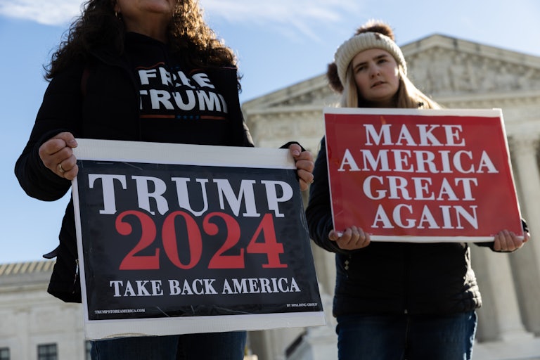 Two women stand outside the Supreme Court holding signs that read "Trump 2024 Take Back America" and "Make America Great Again."